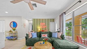 A modern living room with a sectional sofa, a ceiling fan, a striped wall, and a large window with a view. - Resort Style Backyard Tiki Bar Renovated Pool (Largo)