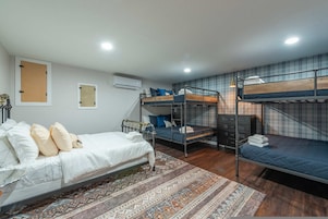 A dormitory room with bunk beds, a single bed, an air conditioning unit, and a patterned rug.
