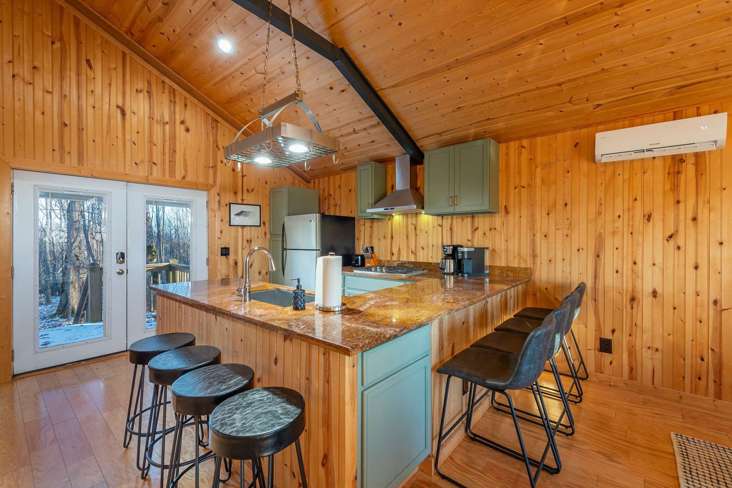 A wooden interior with a kitchen island, bar stools, and a view through a glass door.
