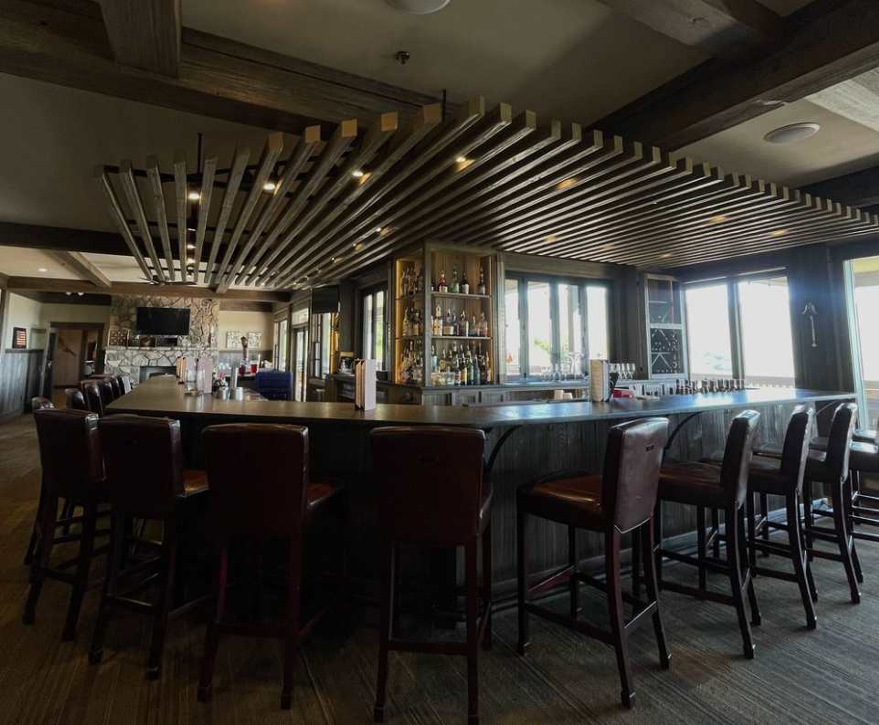 A bar area with a long counter, multiple bar stools, and a wall of liquor bottles.