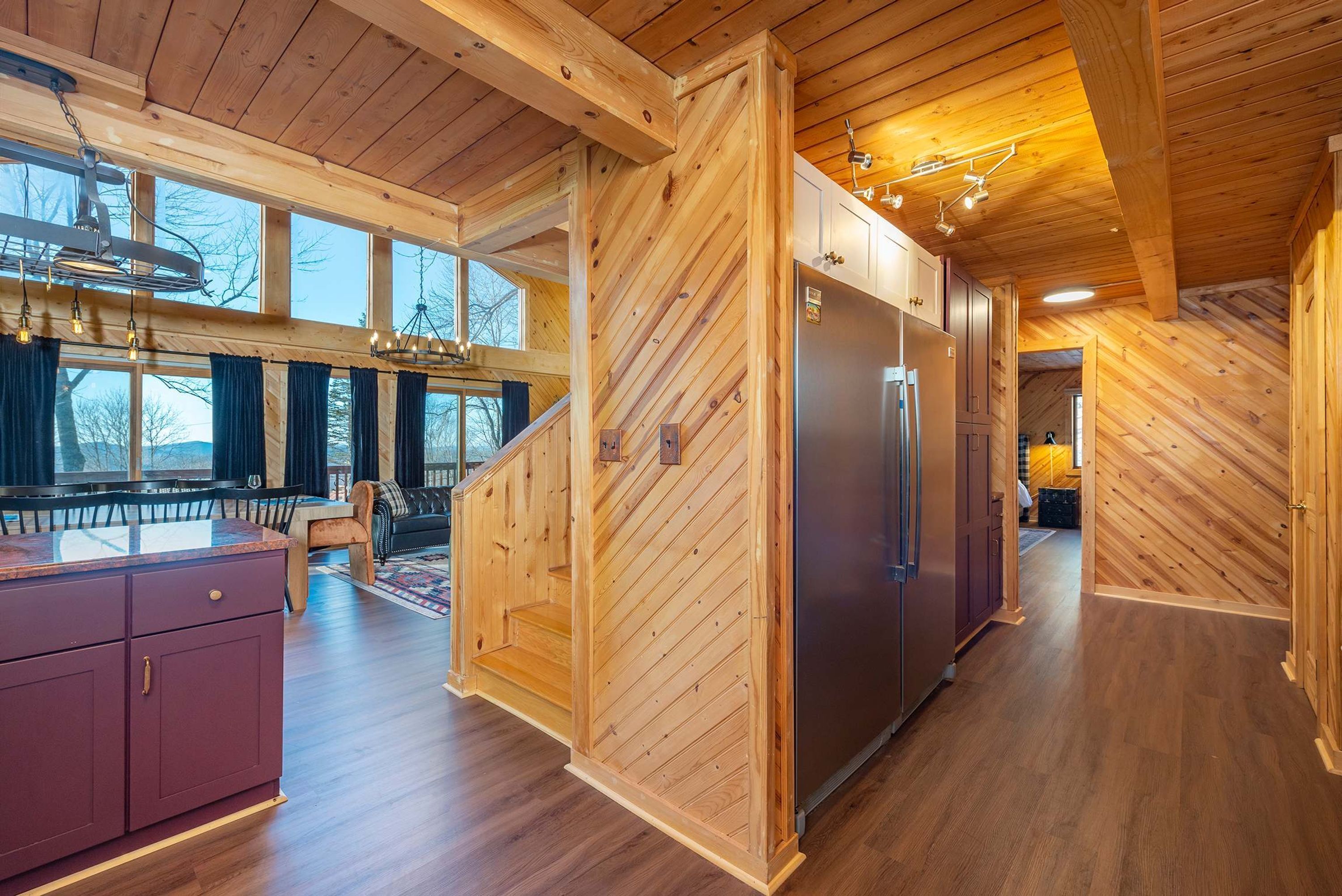 A modern kitchen with a large refrigerator, wooden walls, and a dining area with a view.