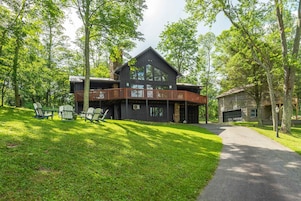 A modern two-story lodge with a wooden deck and a stone garage.