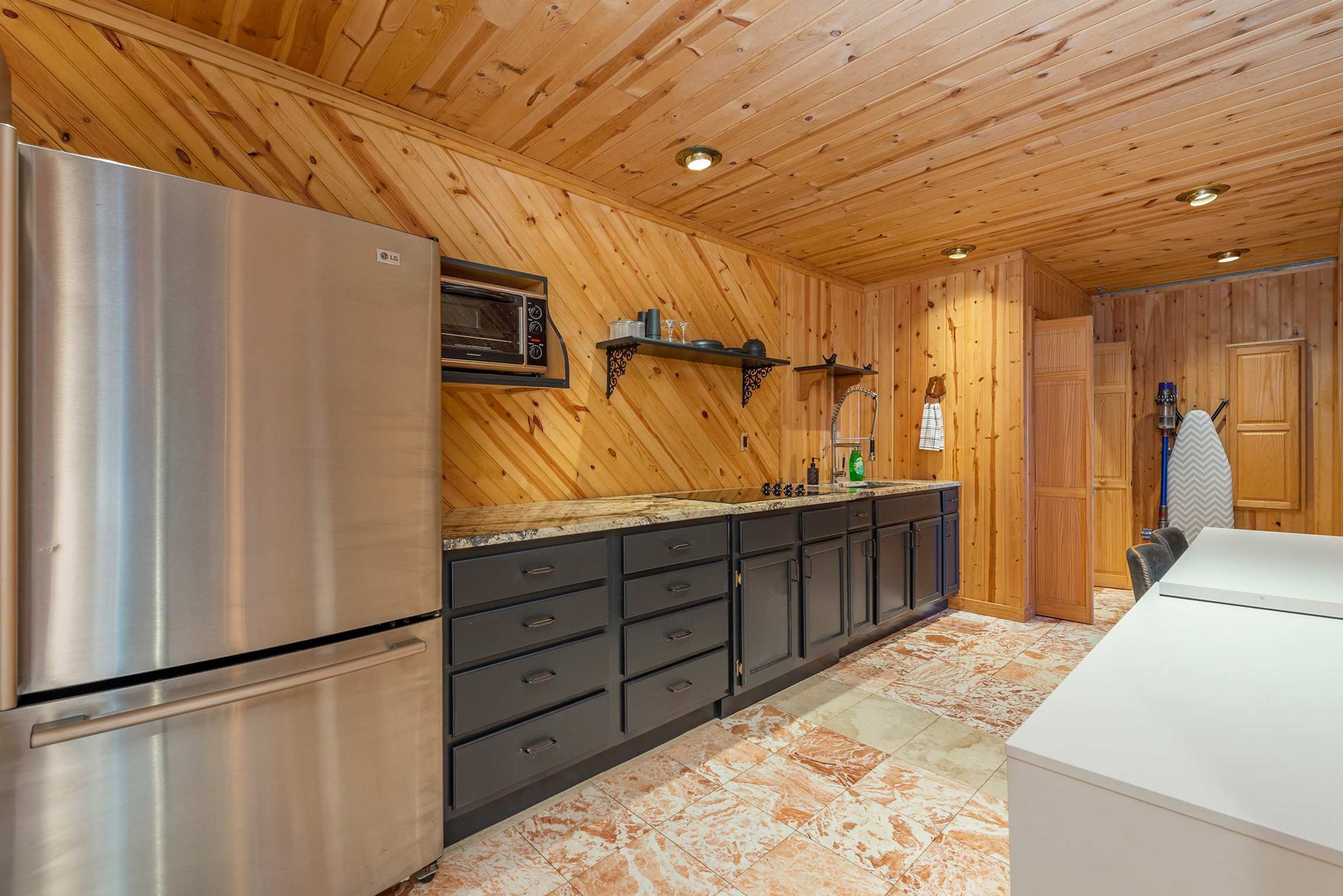 A modern kitchen with wooden paneling, a stainless steel refrigerator, a microwave, and a sink with a marble countertop.