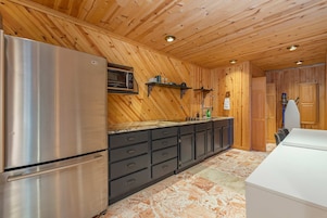 A modern kitchen with wooden paneling, a stainless steel refrigerator, a microwave, and a sink with a marble countertop.