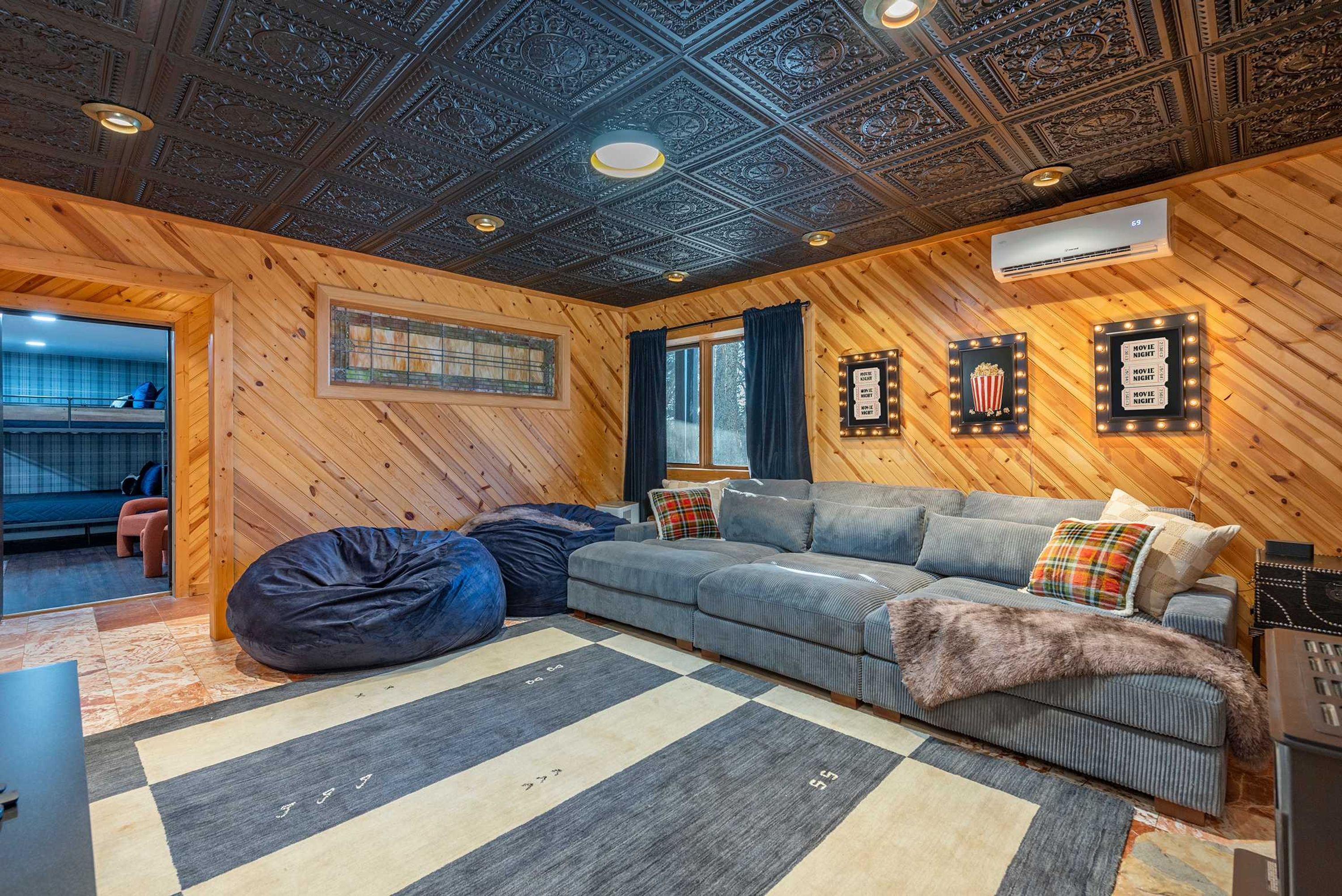 Une pièce chaleureuse avec un plafond en bois, un canapé gris, des fauteuils en forme de poire et un tapis à motifs.