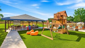 A children's play area with a swing set, seating, and a covered pavilion. - 6k Sqft Estate - Epic Amenities Fun - Sleeps 22 (San Antonio)