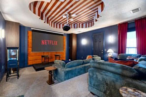 A cozy room with a large screen displaying 'NETFLIX,' a projector, and comfortable seating. - 6k Sqft Estate - Epic Amenities Fun - Sleeps 22 (San Antonio)