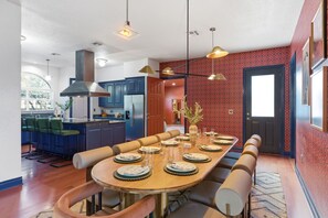 A modern kitchen with blue cabinets, a stainless steel refrigerator, and a dining area with a long wooden table set for six. - 6k Sqft Estate - Epic Amenities Fun - Sleeps 22 (San Antonio)