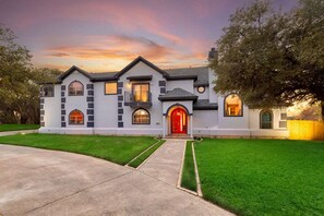 A two-story house with a red front door, multiple windows, and a well-maintained lawn. - 6k Sqft Estate - Epic Amenities Fun - Sleeps 22 (San Antonio)