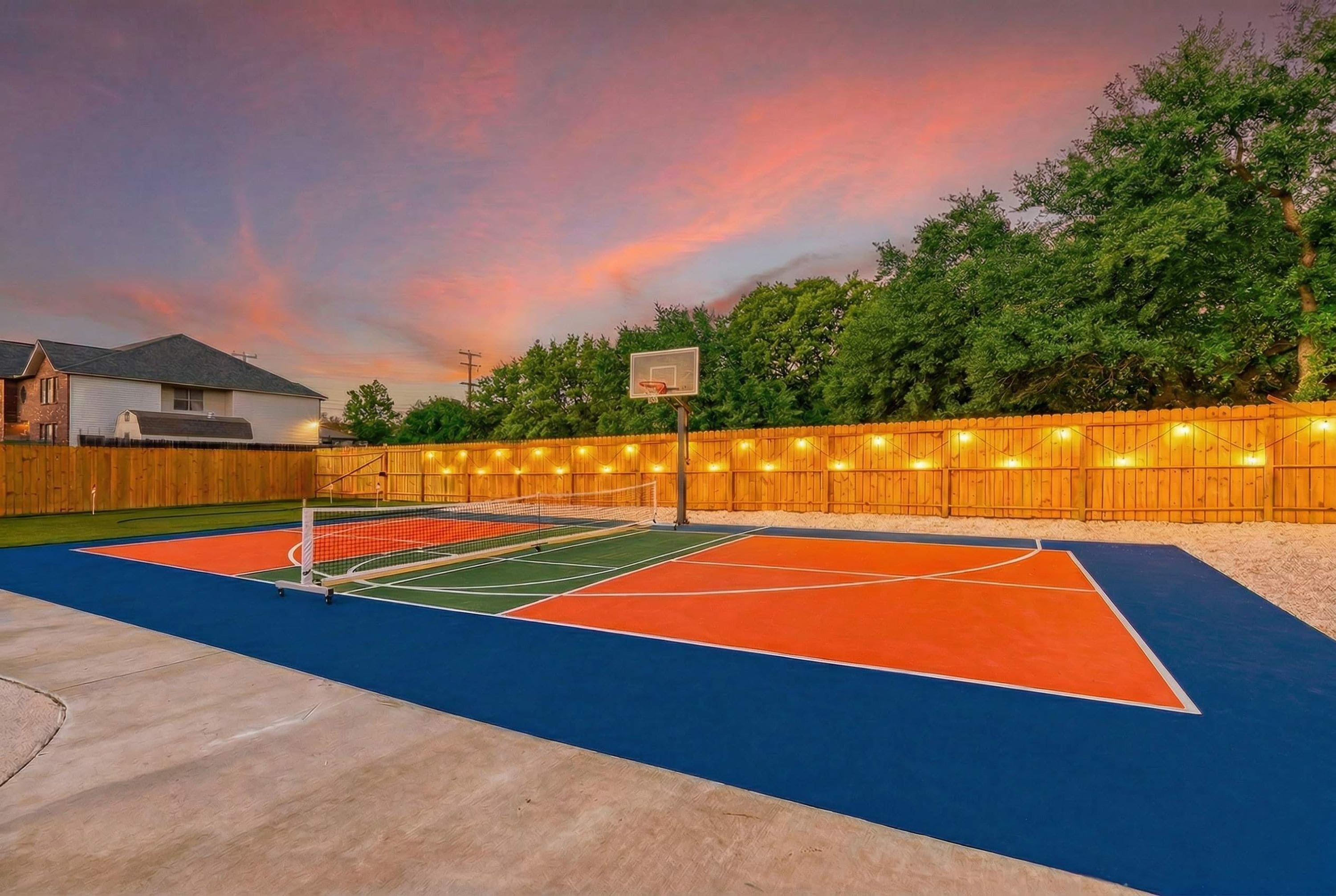 Una cancha de baloncesto al aire libre con una valla de madera y árboles al fondo.