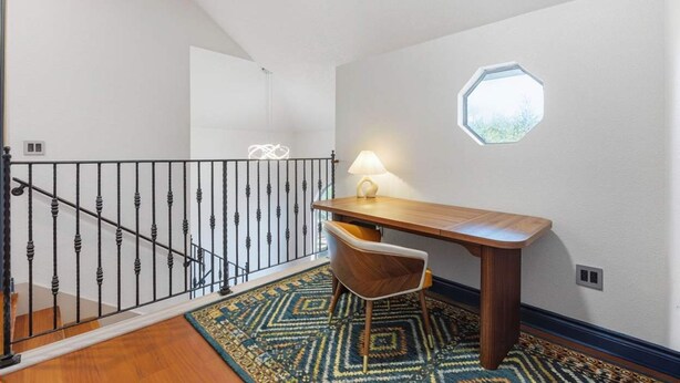 A room with a wooden desk, a chair, a patterned rug, a window, and a black railing. - 6k Sqft Estate - Epic Amenities Fun - Sleeps 22 (San Antonio)