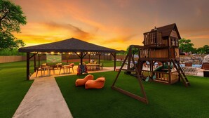 A backyard with a wooden playhouse, a covered seating area, and artificial grass. - 6k Sqft Estate - Epic Amenities Fun - Sleeps 22 (San Antonio)