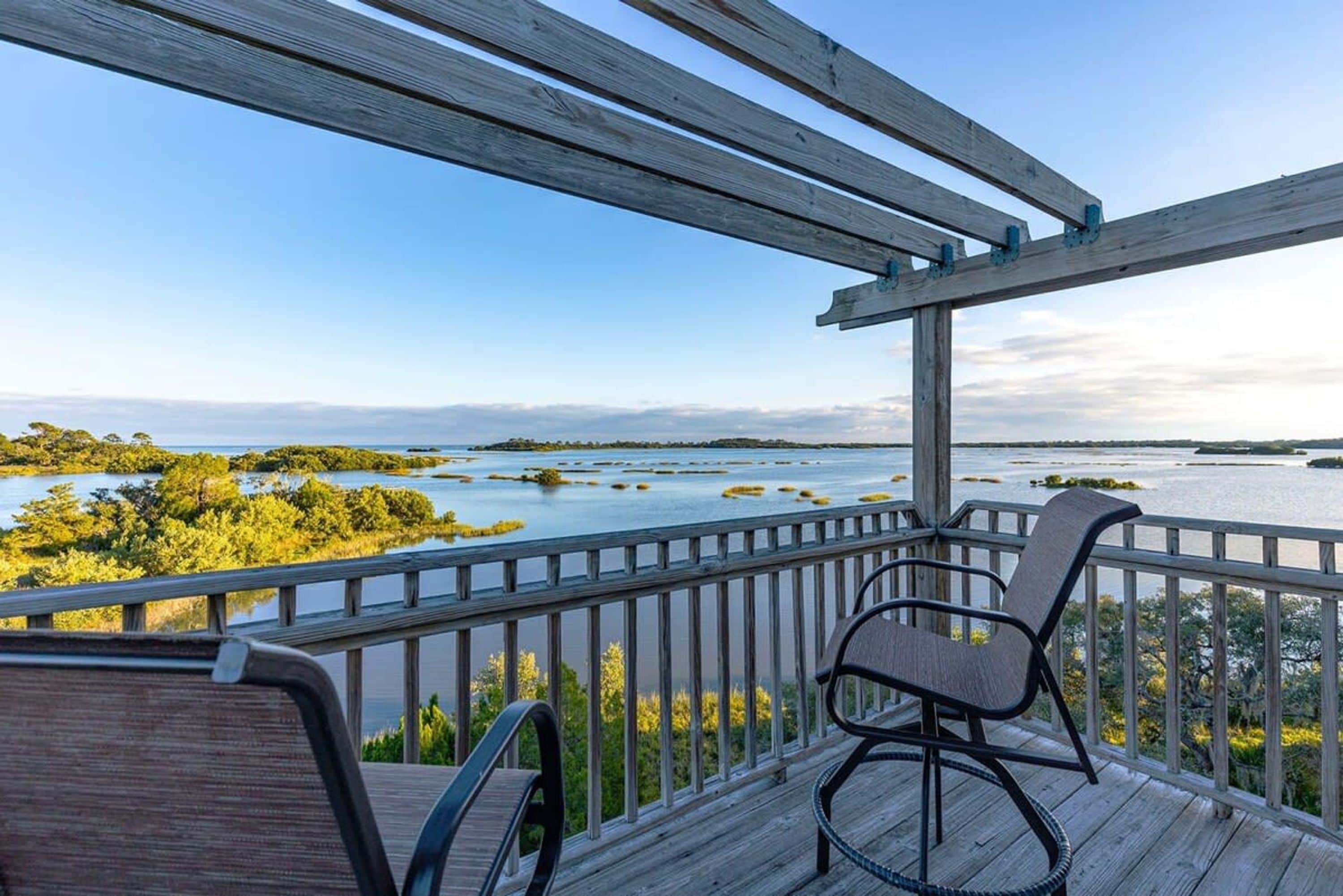 A wooden deck with two chairs overlooking a body of water and land.