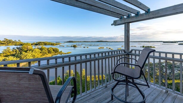 A wooden deck with two chairs overlooking a body of water and land. - 3 Story Haven Fire Pit Kayaks Updated 360 Views (Cedar Key)