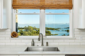 Una cocina con un lavamanos doble, una ventana con vistas a un paisaje natural y una persiana de bambú.