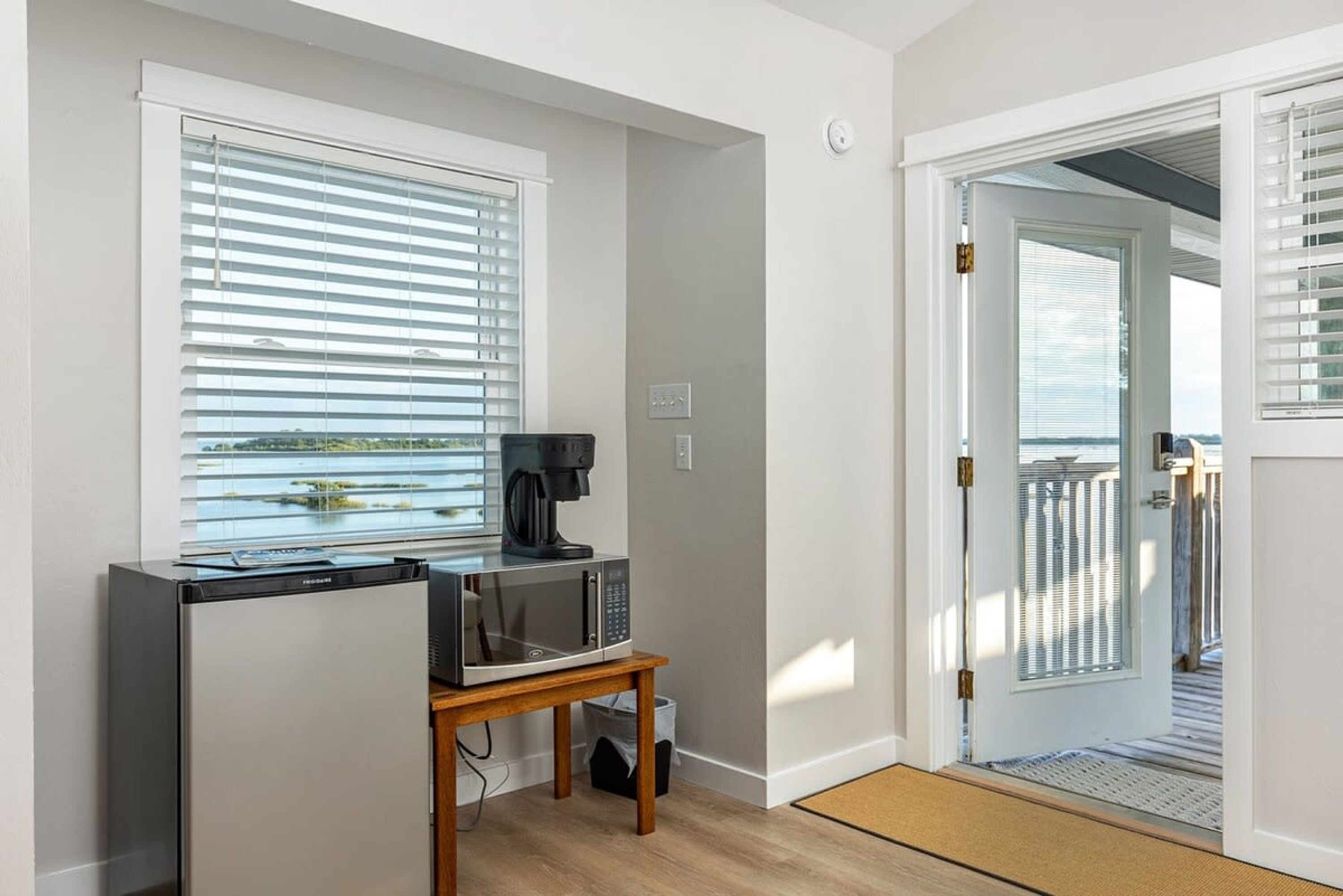 Cocina compacta con refrigerador, microondas y cafetera sobre una mesa de madera.
