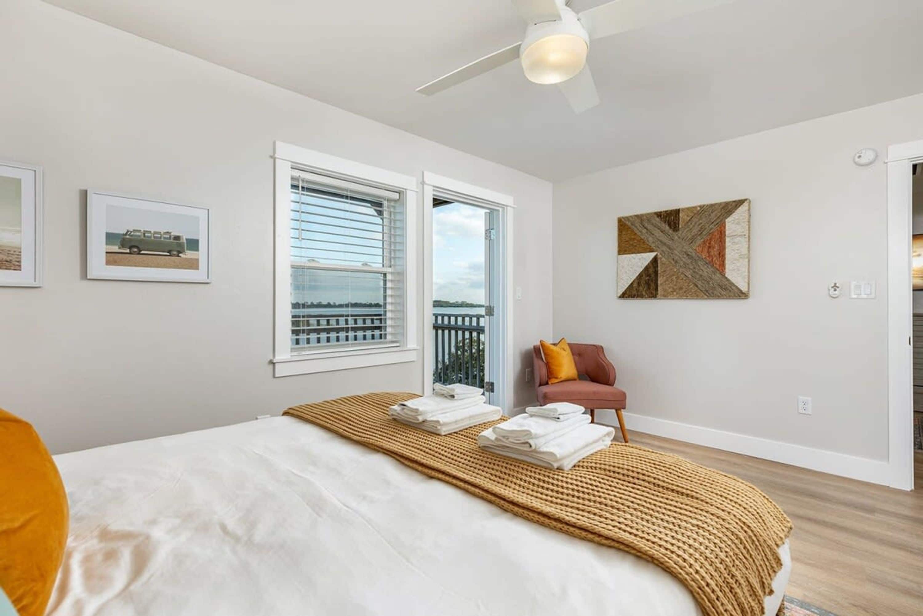 A bedroom with a bed, a window, a ceiling fan, and a painting on the wall.
