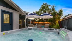 A hot tub with a warning label, surrounded by outdoor seating and umbrellas. - 4 Br Haven Pool Hot Tub Arcade Fire Pit Putt Putt (Largo)