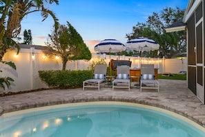 A backyard with a swimming pool, lounge chairs, umbrellas, and string lights. - Poolside Paradise Spa Fire Pit Games (Largo)