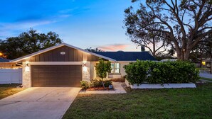 A residential house with a garage, a well-maintained lawn, and a large tree in the front yard. - 4 Br Haven Pool Hot Tub Arcade Fire Pit Putt Putt (Largo)