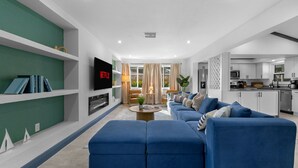 A modern living room with a sectional sofa, a flat-screen TV, and a fireplace. - 4 Br Haven Pool Hot Tub Arcade Fire Pit Putt Putt (Largo)