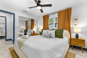 Quarto moderno com uma cama grande, duas mesas de cabeceira, um ventilador de teto e vista para o exterior pela janela.