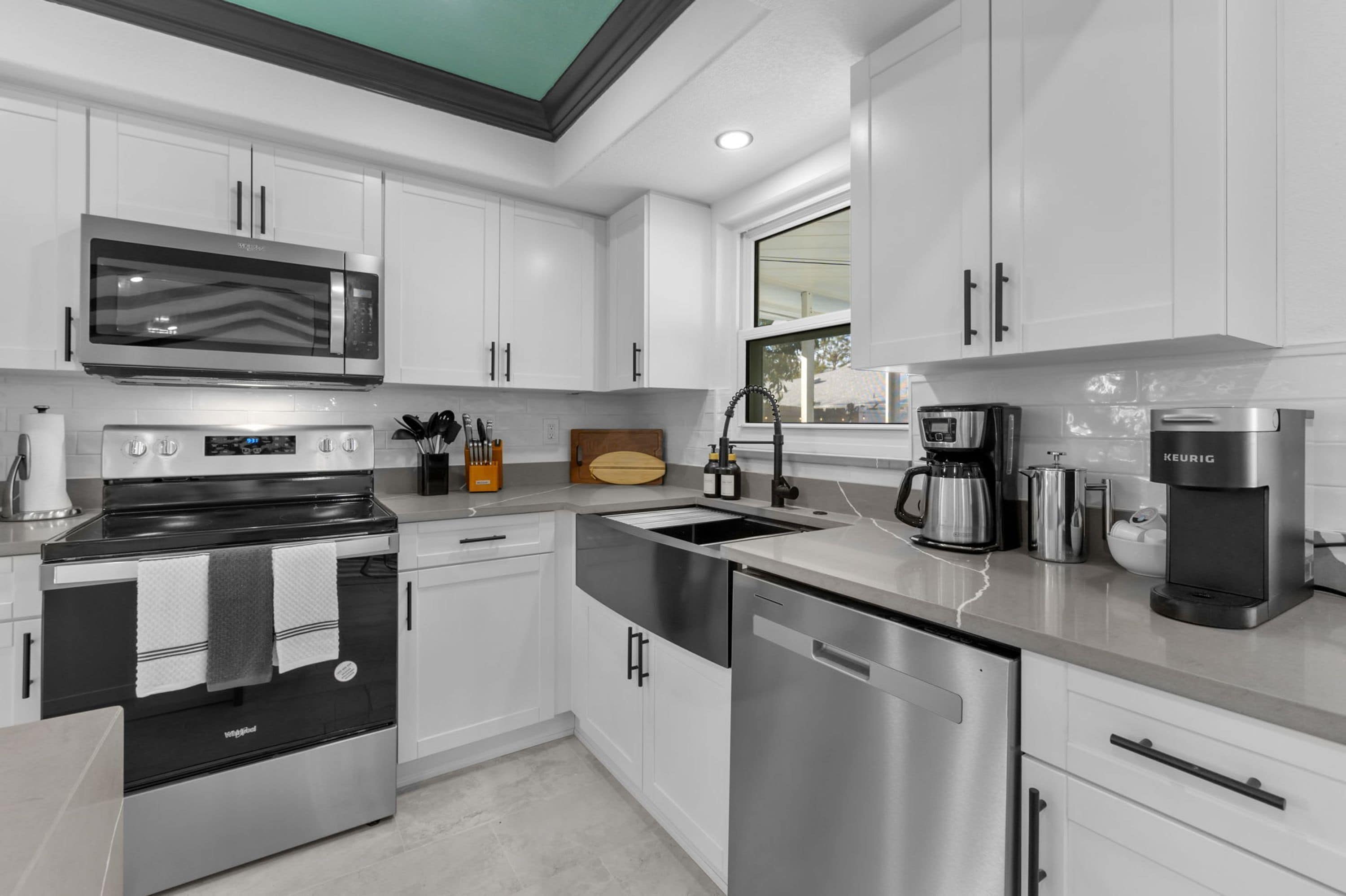 A modern kitchen with stainless steel appliances, white cabinetry, and a window providing natural light.