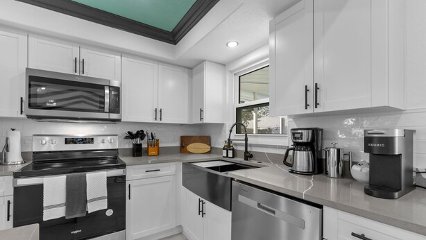 A modern kitchen with stainless steel appliances, white cabinetry, and a window providing natural light. - 4 Br Haven Pool Hot Tub Arcade Fire Pit Putt Putt (Largo)