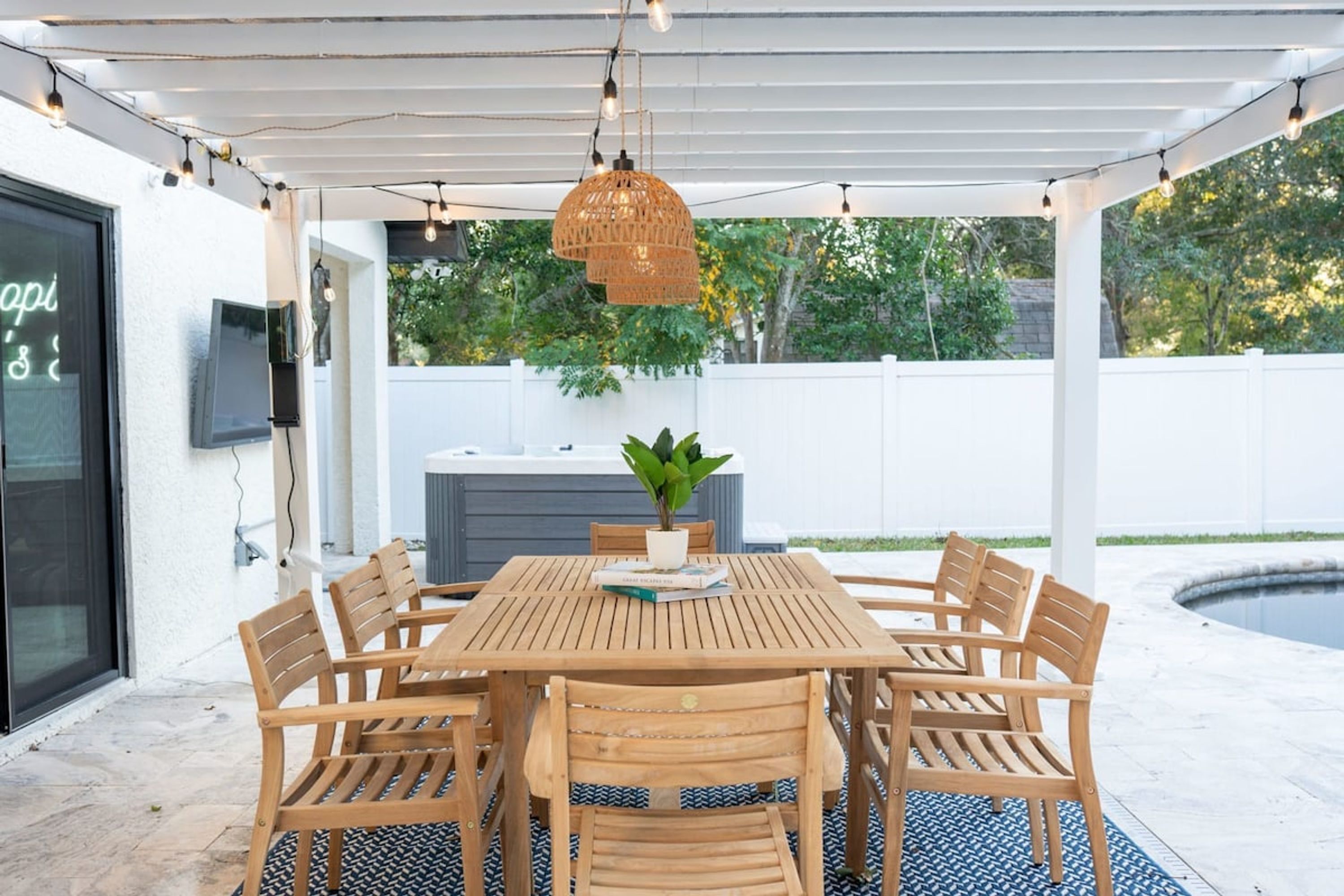Un porche cubierto con una mesa y sillas de madera, una lámpara colgante y una planta en maceta.