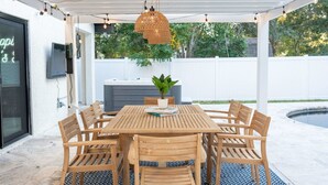 A covered patio with a wooden table and chairs, a hanging light fixture, and a potted plant. - 1 Mile to Honeymoon Island Pool Putt Putt (Palm Harbor)