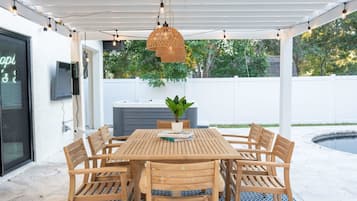 Un porche cubierto con una mesa y sillas de madera, una lámpara colgante y una planta en maceta.