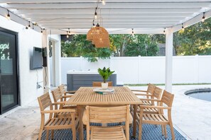 Eine überdachte Terrasse mit Holztisch und Stühlen, einer hängenden Leuchte und einem Blumentopf.