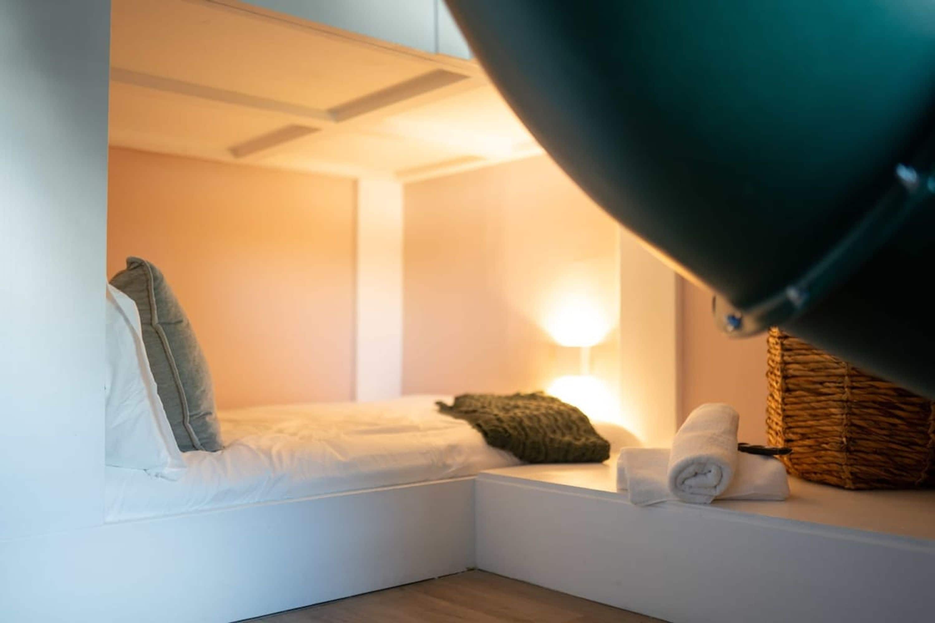 Una habitación pequeña y acogedora con cama, almohada, lámpara y una cesta.