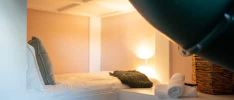 Una habitación pequeña y acogedora con cama, almohada, lámpara y una cesta.