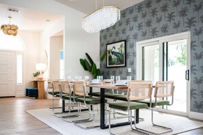 A dining area with a wooden table, green upholstered chairs, and a chandelier. - 1 Mile to Honeymoon Island Pool Putt Putt (Palm Harbor)