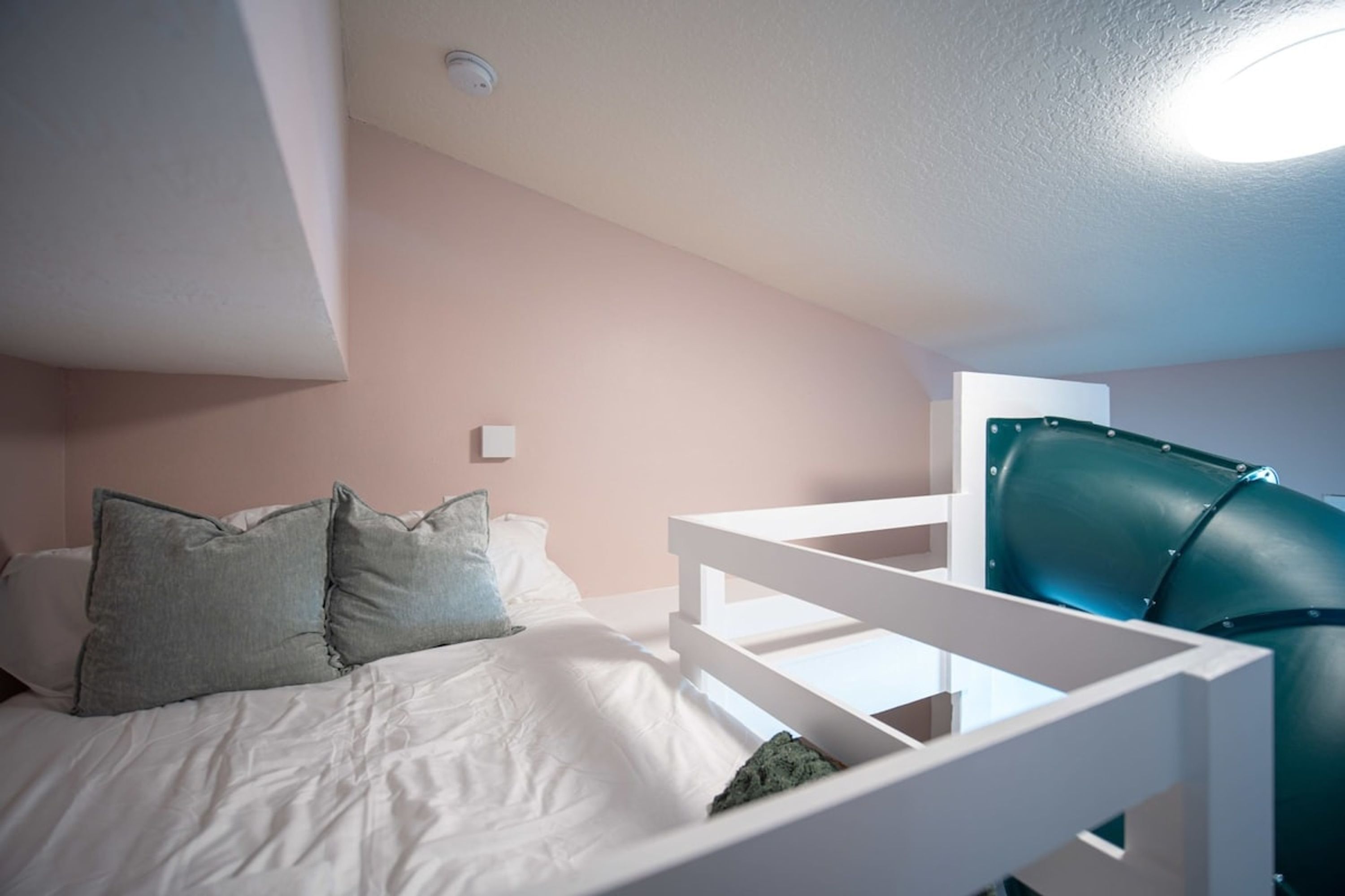 Une chambre à coucher avec un lit, des oreillers, une tête de lit blanche, une chaise verte et un bureau blanc.