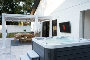 A modern outdoor patio with a hot tub, wooden furniture, and a TV mounted on the wall. - 1 Mile to Honeymoon Island Pool Putt Putt (Palm Harbor)