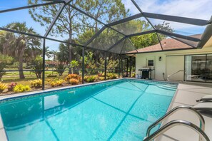 Une piscine dotée d’une structure en verre, entourée de jardins aménagés et d’arbres.