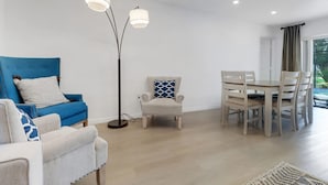 A modern living room with a blue sofa, a white armchair, a dining table with chairs, and a floor lamp. - High Tide - 3 Br Sleeps 6 - Private Pool - Games (Naples)