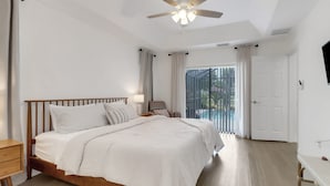 A bedroom with a wooden bed, a nightstand, a desk, a ceiling fan, and a view of a pool through a glass door. - High Tide - 3 Br Sleeps 6 - Private Pool - Games (Naples)