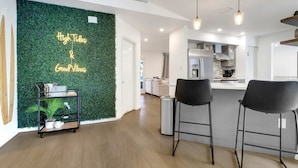 A modern kitchen with a bar area, a green wall with text, and a cart with items. - High Tide - 3 Br Sleeps 6 - Private Pool - Games (Naples)