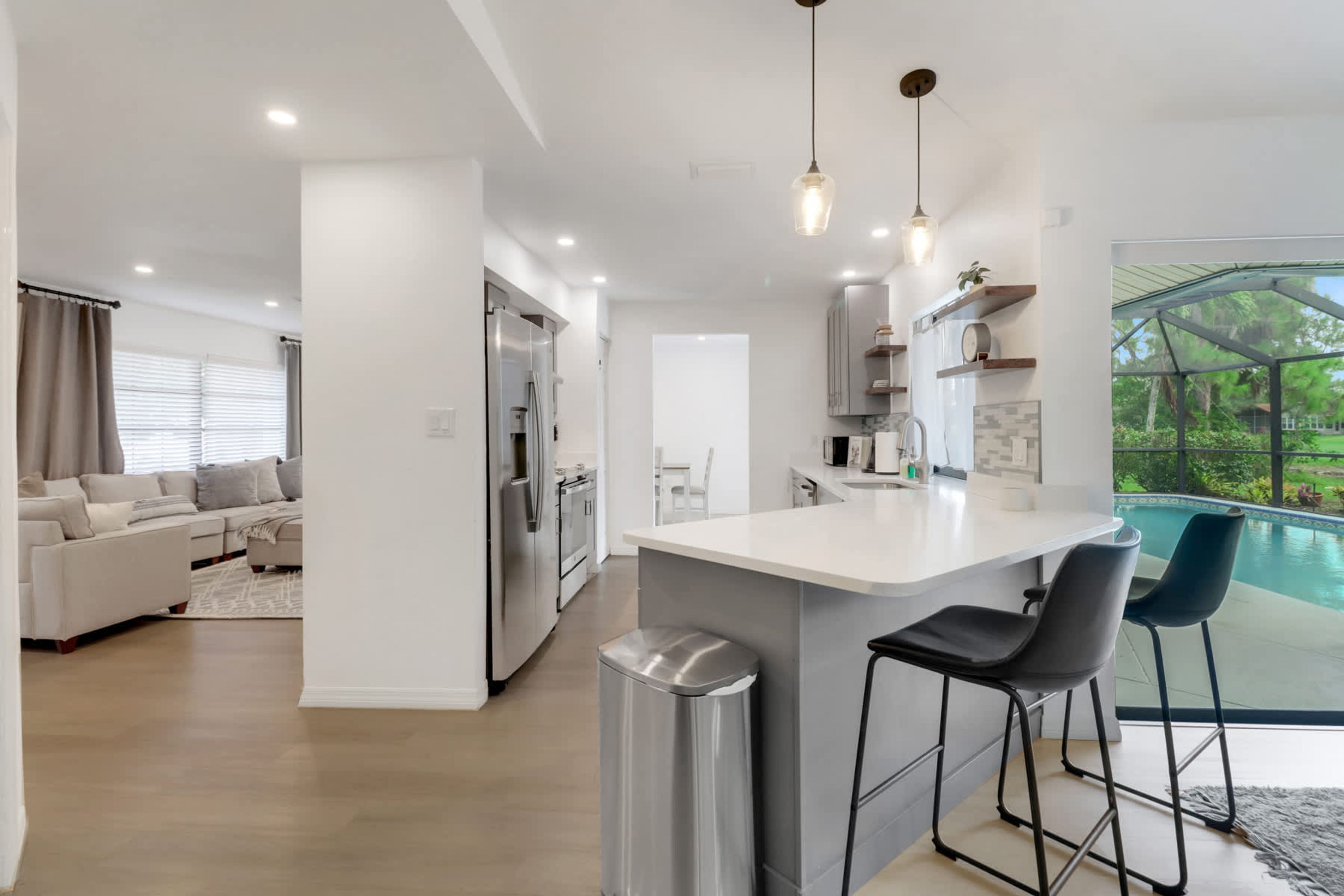 A modern kitchen with a central island, bar stools, and a view of a swimming pool.