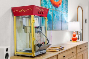 A food vending machine with a red and yellow design, placed on a wooden counter with a painting and a lamp in the background. - The Painted Paddle Pool Hottub Pickleball Court (Lake Dallas)