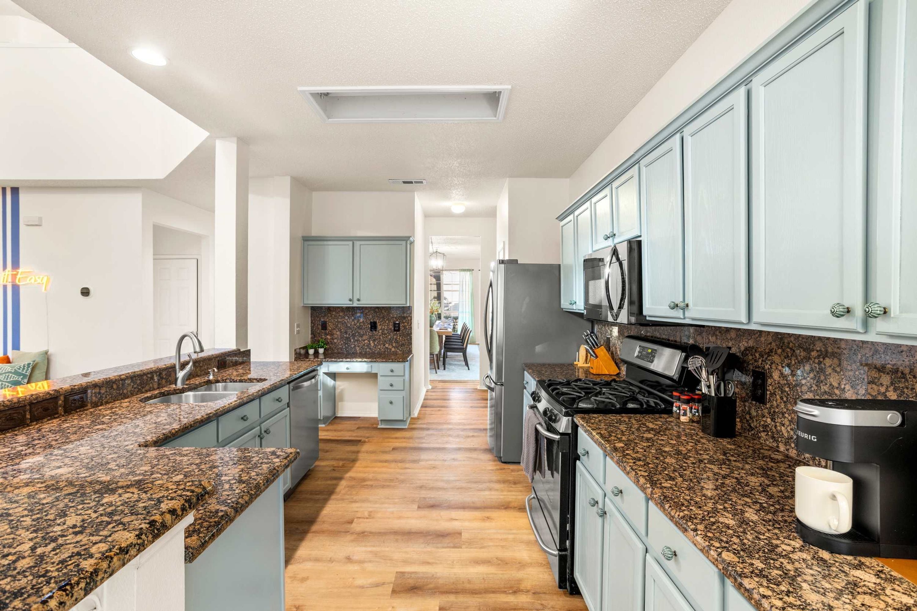 A modern kitchen with granite countertops, stainless steel appliances, and light blue cabinetry.