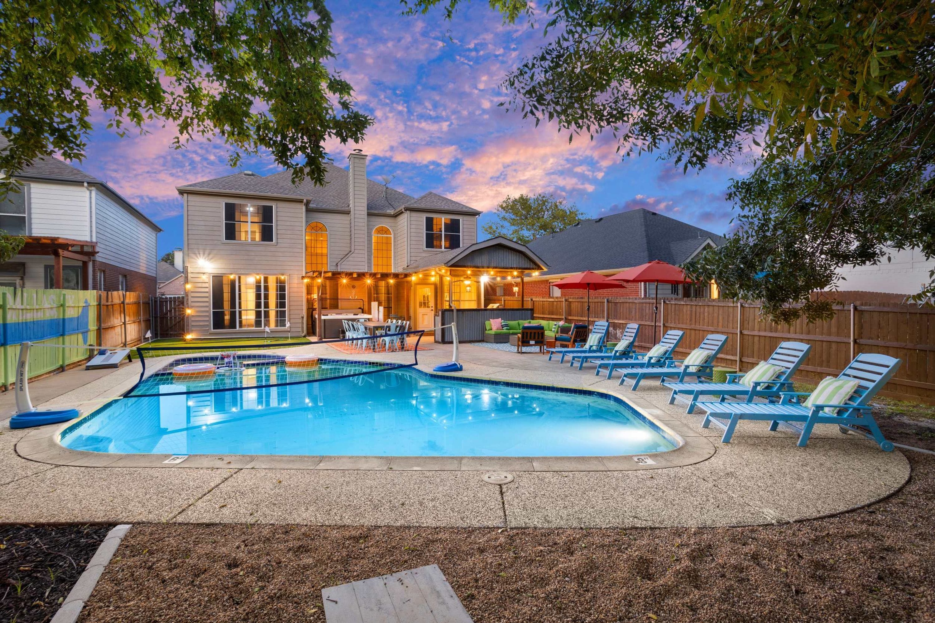 A backyard with a swimming pool, lounge chairs, and a covered patio area.