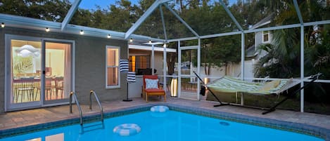 A swimming pool with a glass enclosure, a hammock, and outdoor furniture.