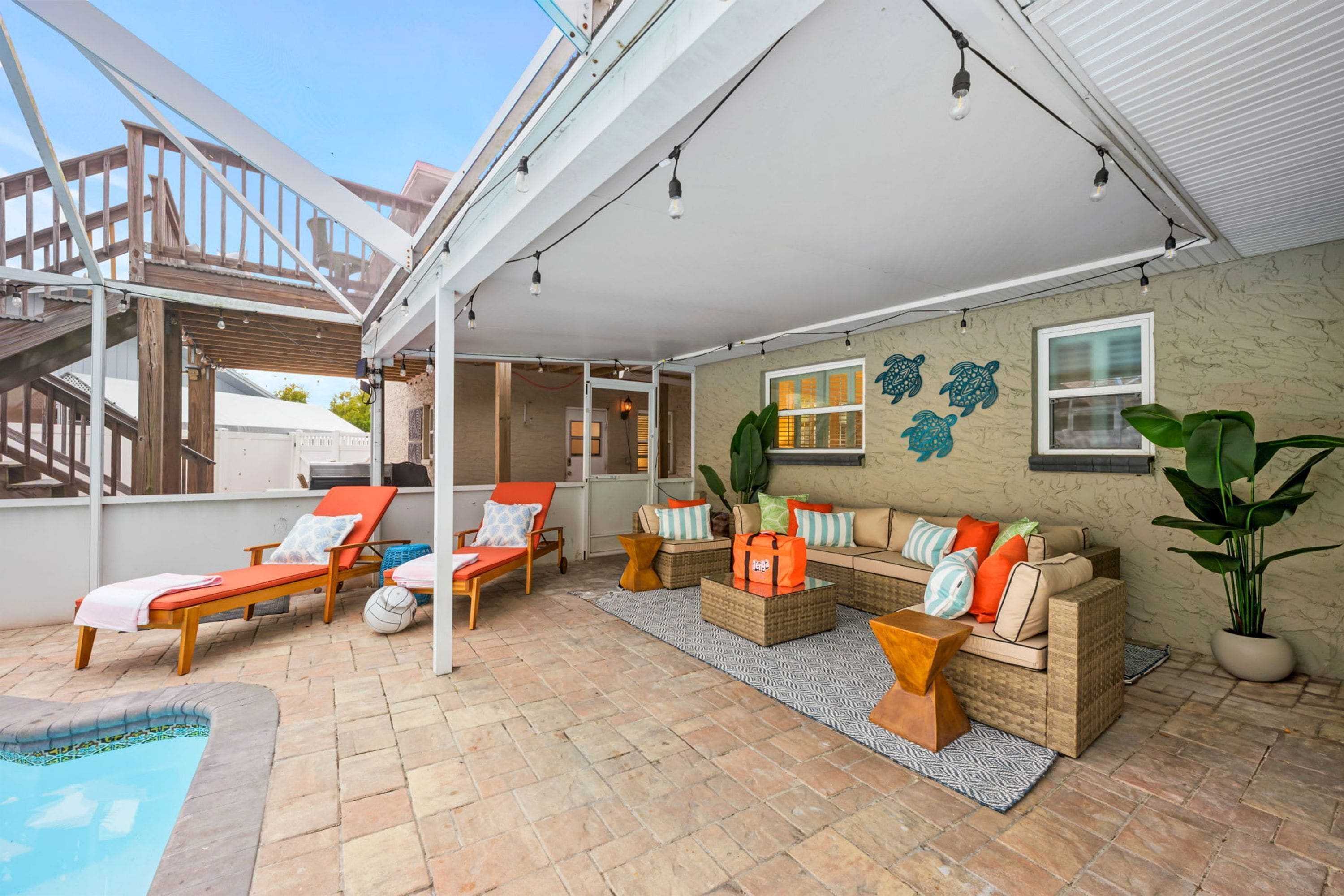 An outdoor living area with a pool, lounge chairs, a sofa set, and decorative wall art.