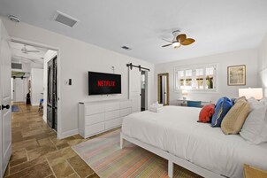 Quarto com cama, televisão na parede, ventoinha no teto e janela com persianas.