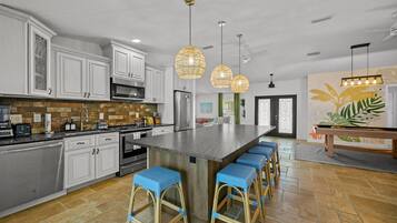 Una cocina moderna con armarios blancos, una isla grande con taburetes de bar e iluminación colgante.