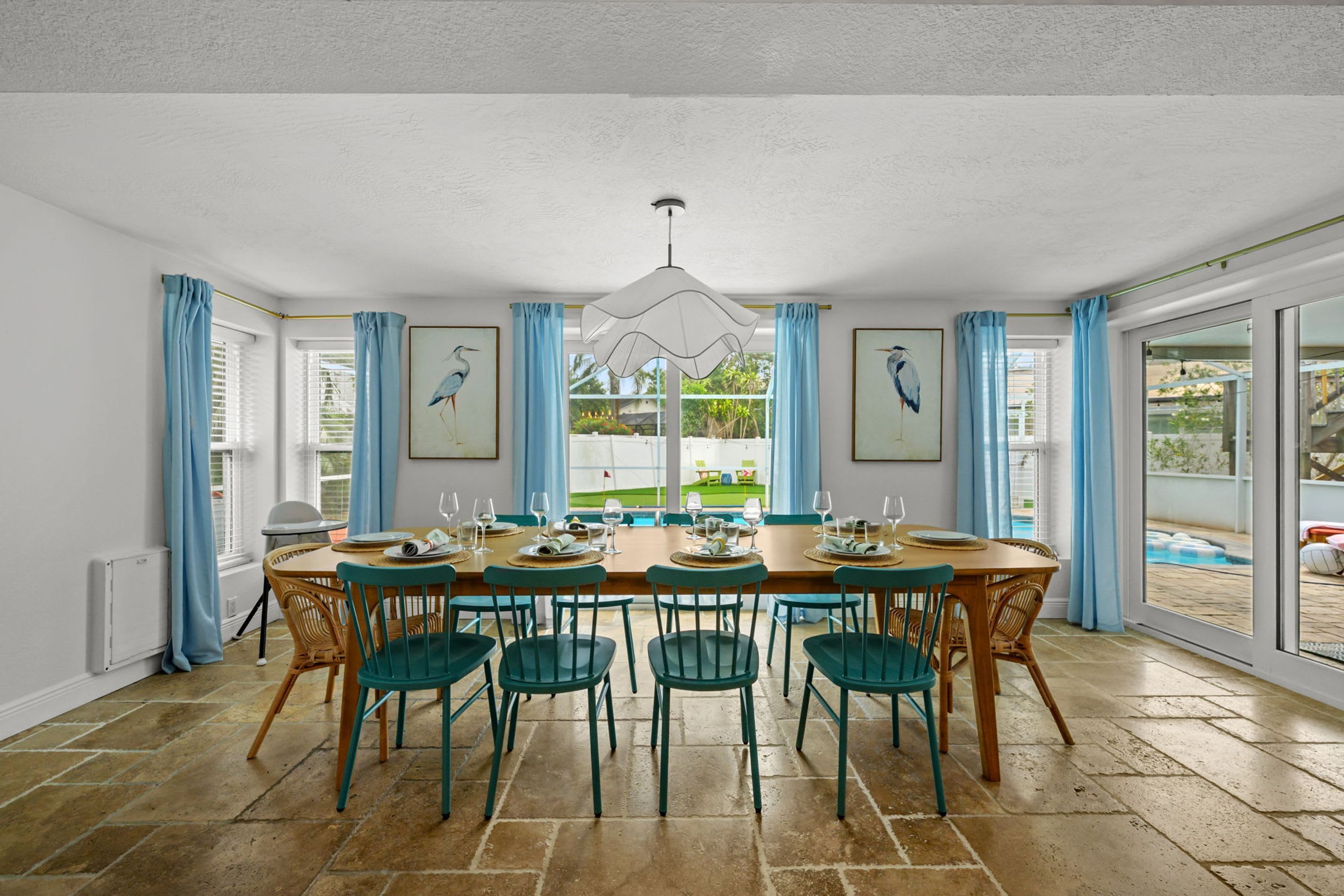 A dining area with a table set for six, surrounded by chairs, with a view of a pool and greenery outside.